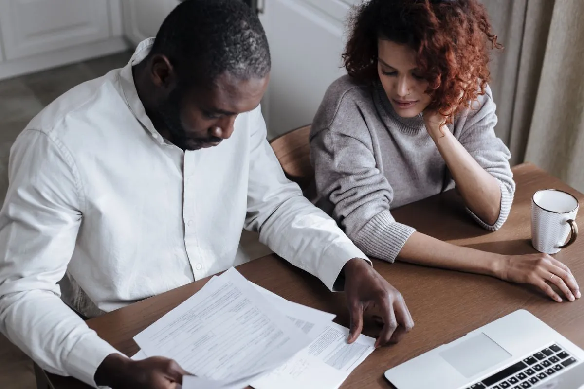 Un couple relit des documents ensemble à un bureau, un ordinateur portable ouvert à côté