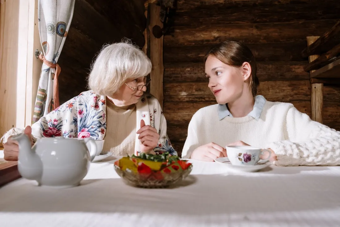 Une femme âgée et une jeune femme discutent à table autour d'une théière et de tasses de thé